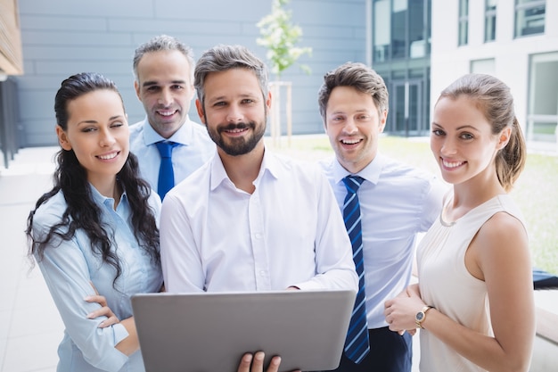 Confident businesspeople standing outside office building with laptop