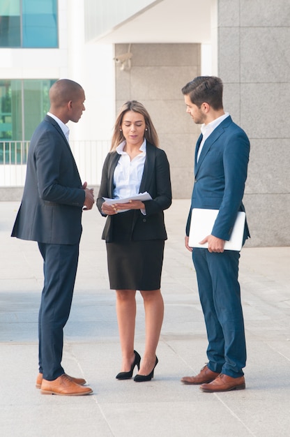 Confident businesswoman talking to male colleagues outdoors