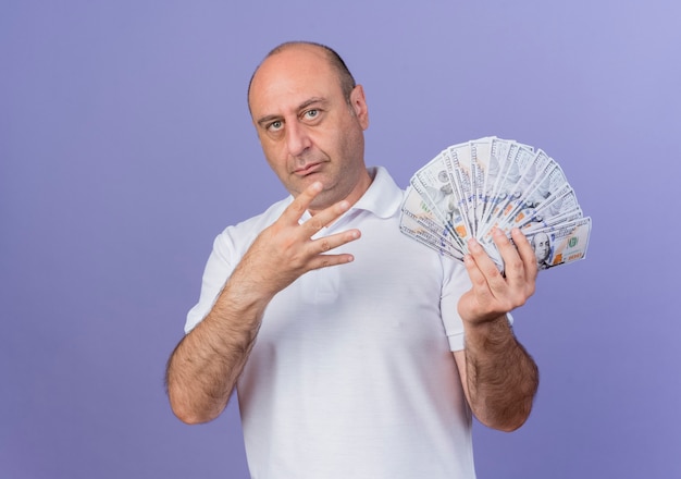Уверенный случайный зрелый бизнесмен, держащий деньги и показывающий четыре рукой, изолированной на фиолетовом фоне с копией пространства