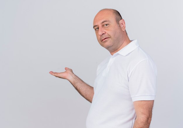 Confident casual mature businessman standing in profile view looking at camera and pointing with hand at side isolated on white background with copy space