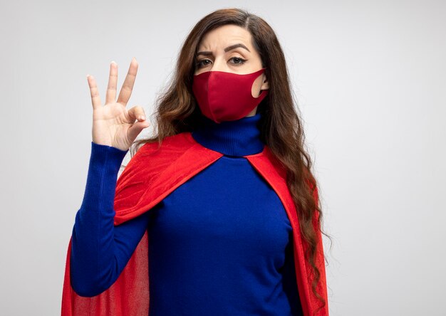 Confident caucasian superhero girl with red cape wearing red protective mask