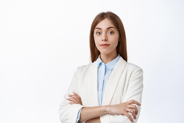비즈니스 정장을 입은 자신감 있는 CEO 여성은 가슴에 팔짱을 낀 모습으로 전문적인 흰색 배경처럼 서 있는 카메라 앞에서 단호하고 준비가 되어 있습니다.