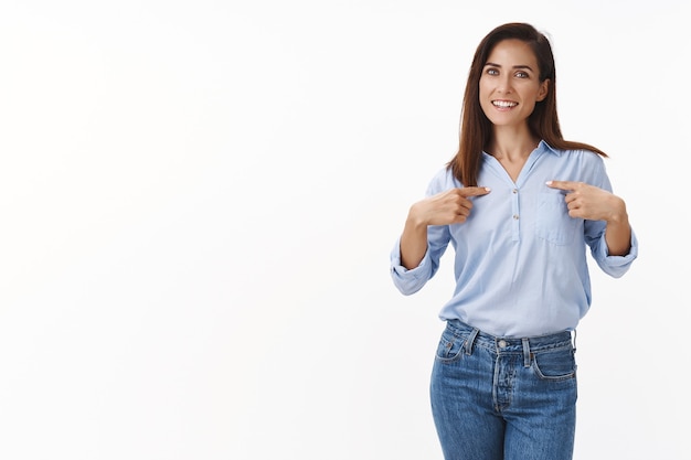 Fiduciosa allegra madre europea femminile che indica se stessa, indica il corpo, vantarsi dei propri successi, sorridere, aiutare volontario a gestire gli affari, sorridere felice, stare in piedi sicuro di sé muro bianco