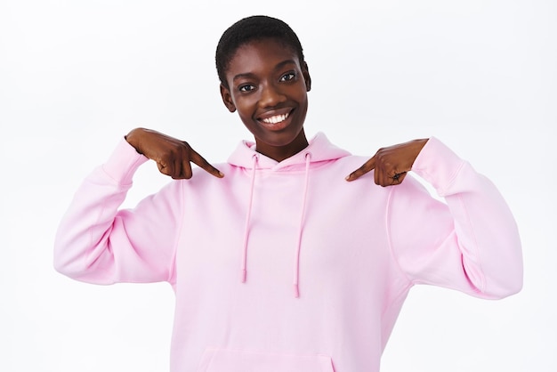 Confident cool african-american woman in pink hoodie, smiling and looking camera assertive as talking about herself