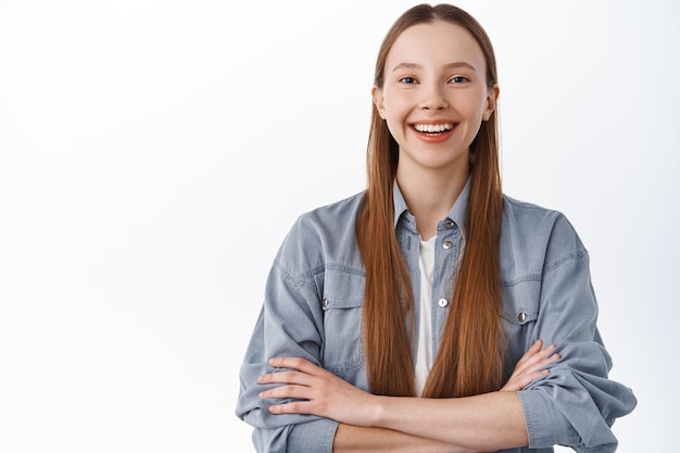 Confident and determined young girl, student cross arms on chest power pose, smiling and looking self-assured, standing over white background near your logo, place for banner