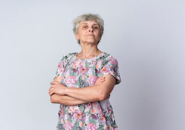 Confident elderly woman crosses arms and looks isolated on white wall