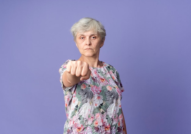 Бесплатное фото Уверенная пожилая женщина протягивает кулак на фиолетовой стене