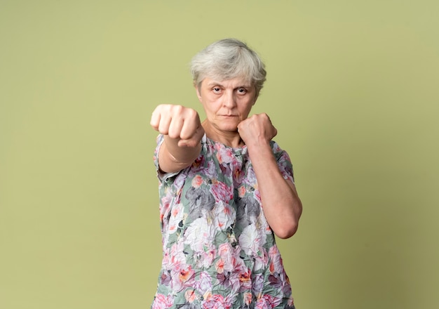 Free photo confident elderly woman keeps fists ready to punch isolated on olive green wall