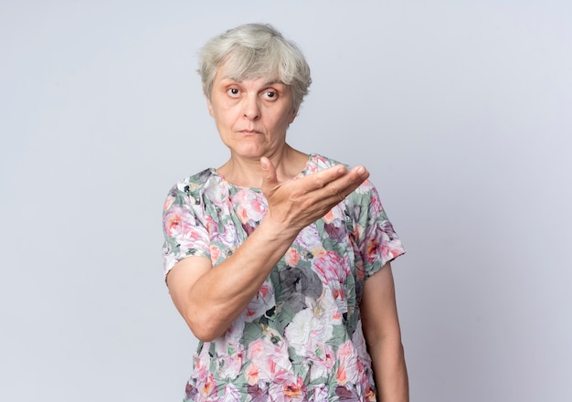 Confident elderly woman points at side with hand isolated on white wall