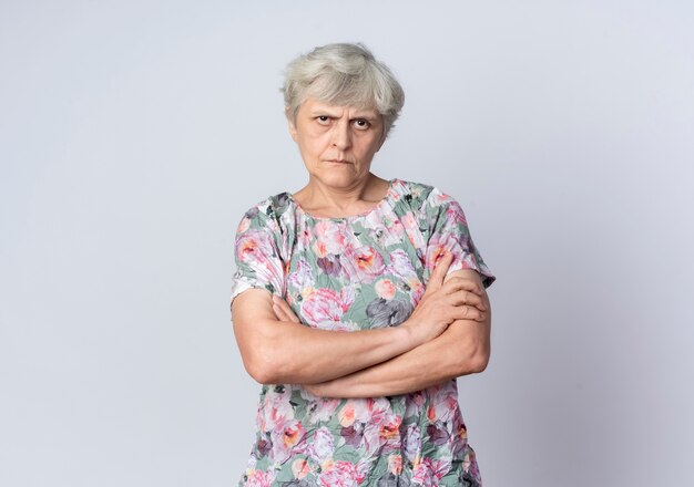 Confident elderly woman stands with crossed arms isolated on white wall