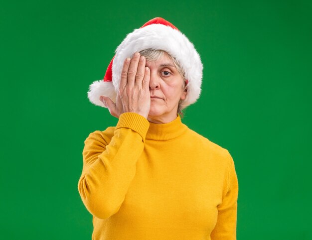 복사 공간 보라색 배경에 고립 된 손으로 그녀의 눈을 덮고 산타 모자와 자신감이 노인 여성