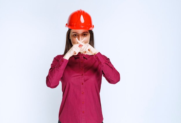 Confident female architect in red hard helmet showing stop sign. 