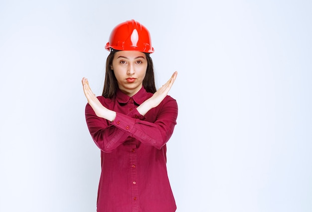 Confident female architect in red hard helmet showing stop sign. 