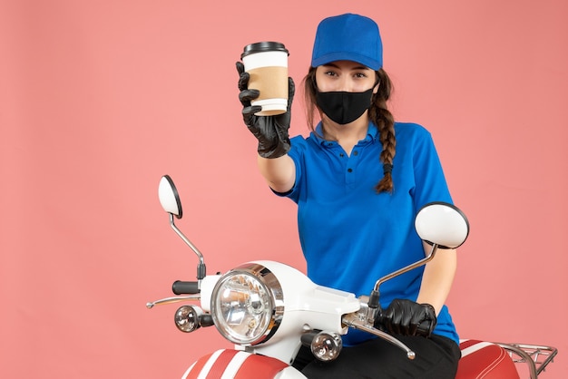Confident female courier wearing black medical mask and gloves delivering orders on peach background