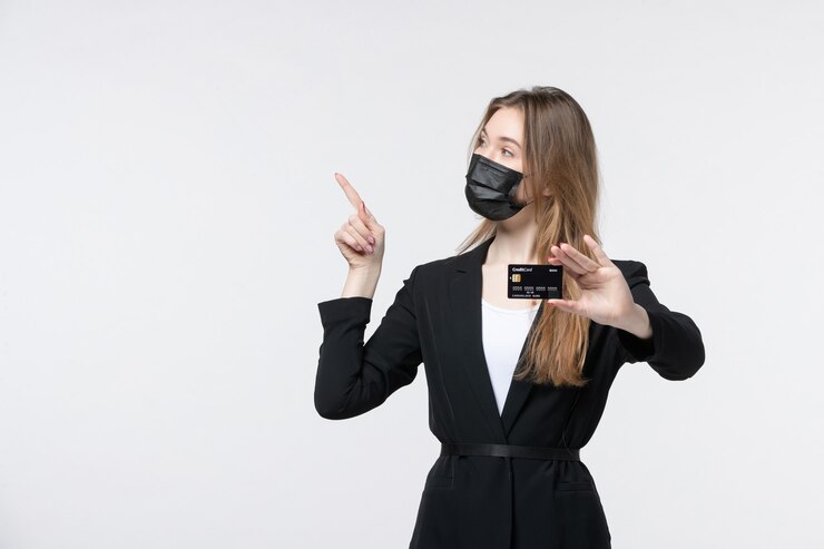 Бесплатный Фотография уверенная женщина-предприниматель в костюме, одетая в медицинскую маску и показывающая банковскую карту, указывающую вверх на белом