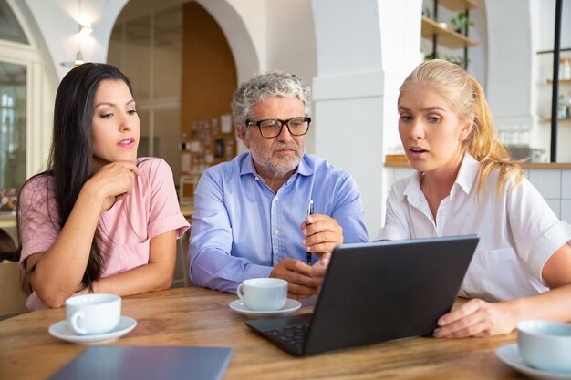 Confident female manager showing presentation on laptop to young woman and mature man, speaking and explaining details