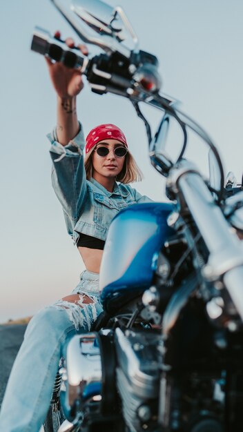 Уверенная женщина в джинсовой одежде и красной бандане позирует на мотоцикле