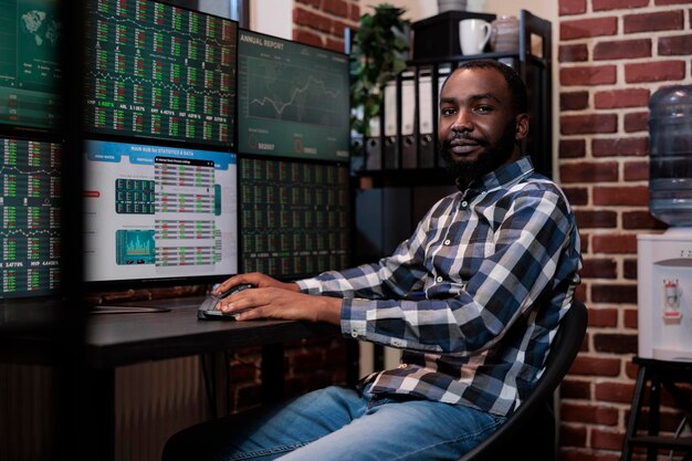 Confident forex stock trader sitting at workstation with multiple displays showing real time financial data. Hedge fund trader day trading at night while sitting investment agency office.