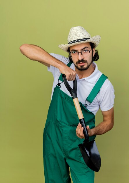 Confident gardener man in optical glasses wearing gardening hat holds spade