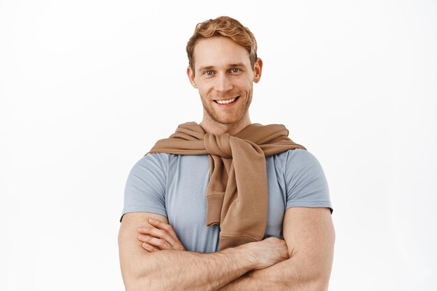 Confident ginger man with strong masculine body, sportsman in casual clothes cross arms on chest, smiling professional, look determined and happy, standing over white background