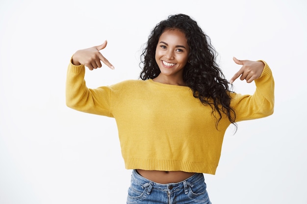 Confident girl talking about herself, bragging awesome achievement pointing chest and smiling self-assured, boastfully showing-off, standing white wall pleased, gain success