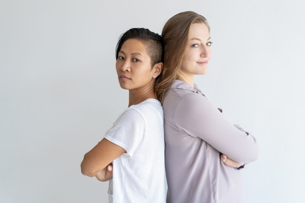 Confident girls standing back to back with arms crossed