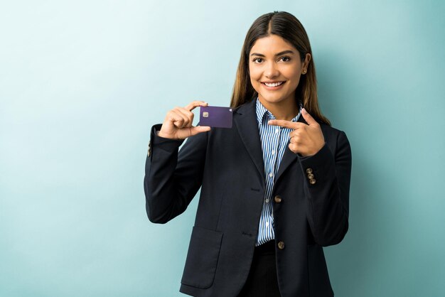 Confident good looking female entrepreneur pointing at her credit card against isolated background