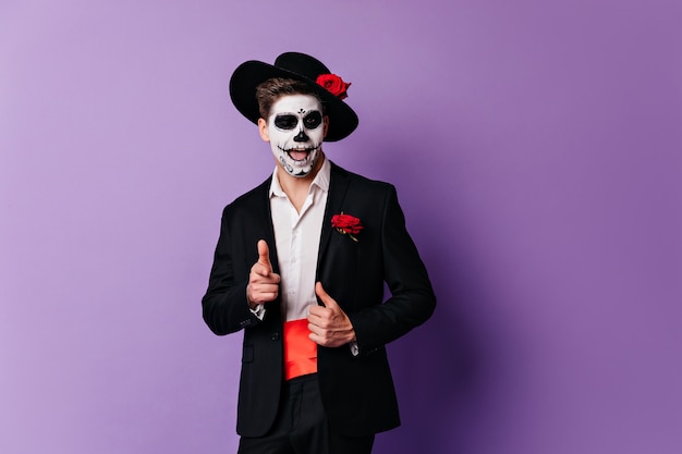 Confident guy in zombie attire posing on purple background. Good-looking deadman enjoying halloween party.