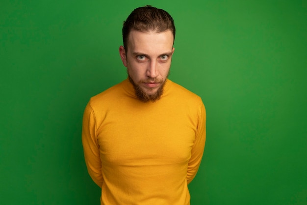 Confident handsome blonde man looks at front isolated on green wall