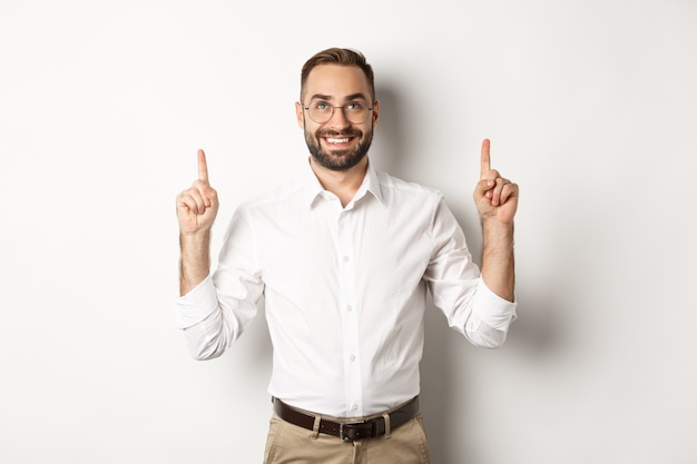 Confident handsome businessman showing logo, pointing and looking up at announcement, standing  