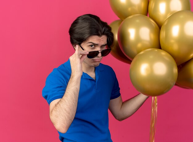 Confident handsome caucasian man in sun glasses holds helium balloons looking at camera 