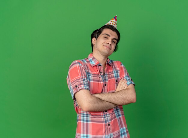 Confident handsome caucasian man wearing birthday cap stands with crossed arms 