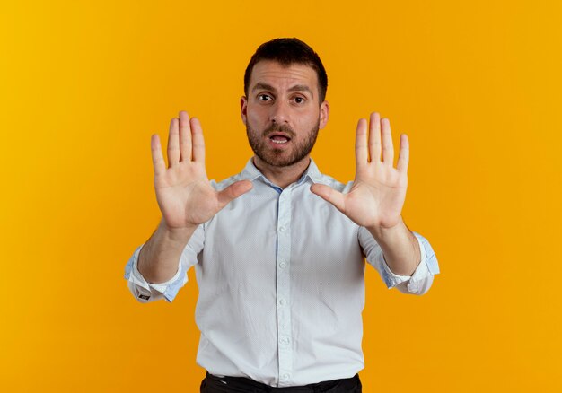 自信を持ってハンサムな男のジェスチャーは、オレンジ色の壁に分離された両手で一時停止の標識