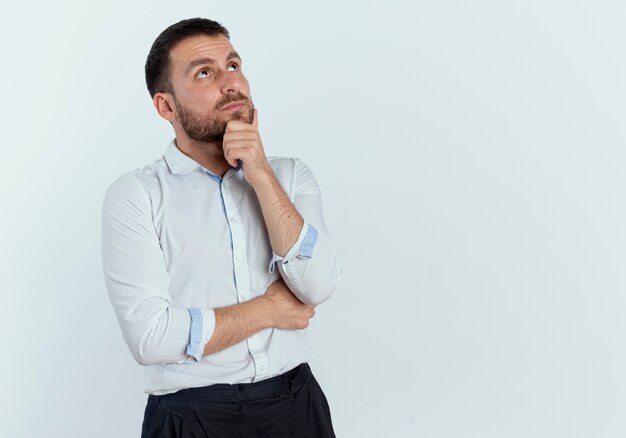 Confident handsome man holds chin and looks up isolated on white wall