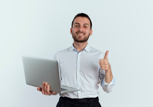 Confident handsome man holds laptop thumbs up isolated on white wall