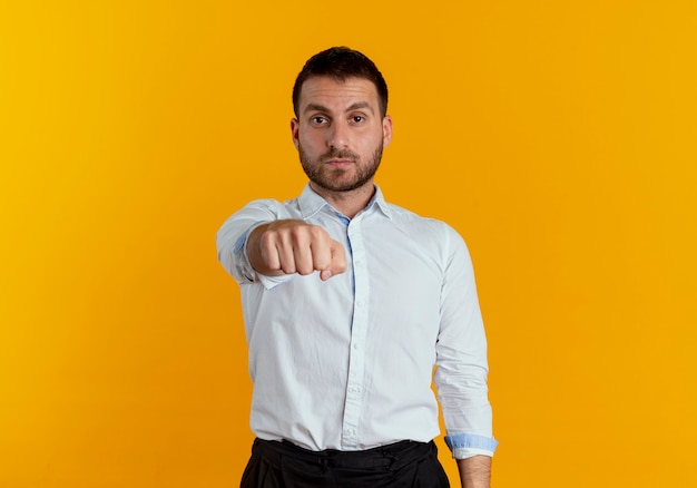 Confident handsome man holds out fist isolated on orange wall