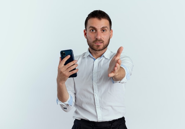 Confident handsome man holds phone stretching out hand isolated on white wall