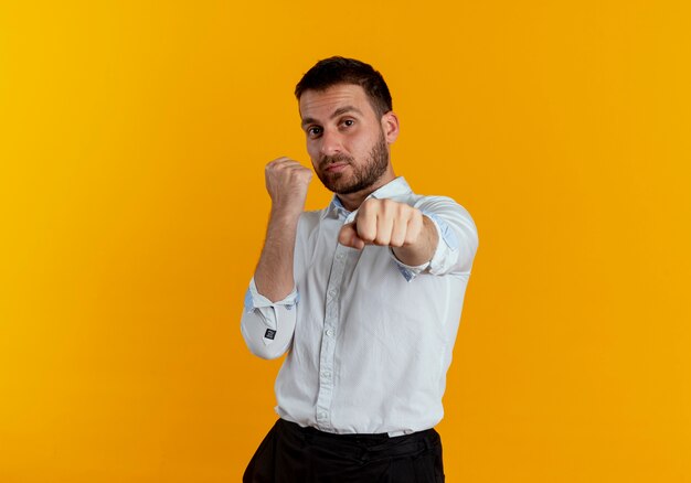 Confident handsome man keeps fists ready to punch isolated on orange wall