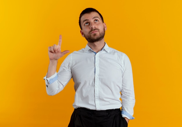 Confident handsome man looks and points up isolated on orange wall