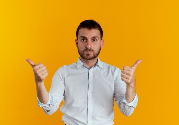 Confident handsome man points at side with hands isolated on orange wall