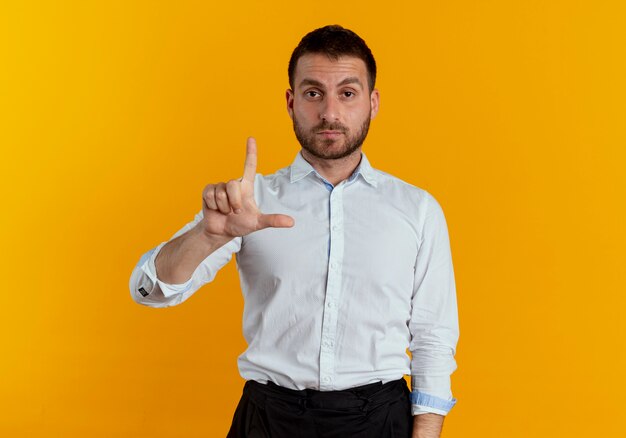 Confident handsome man points up isolated on orange wall