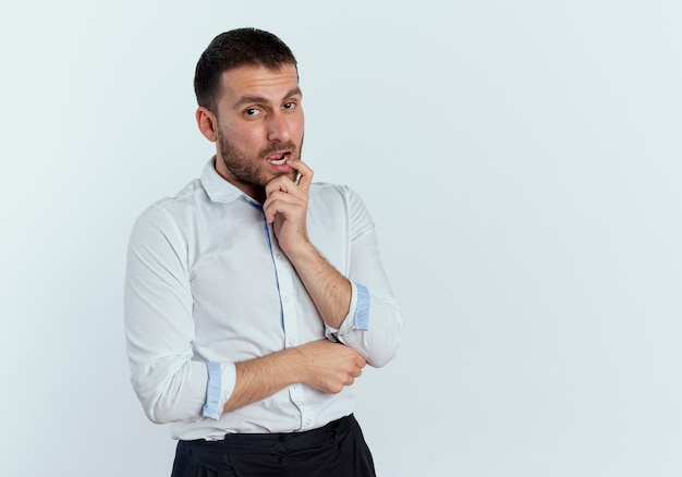 Confident handsome man puts finger on mouth looking isolated on white wall