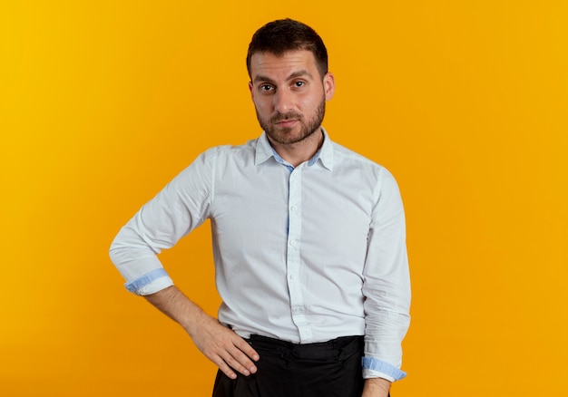 Confident handsome man puts hand on waist isolated on orange wall