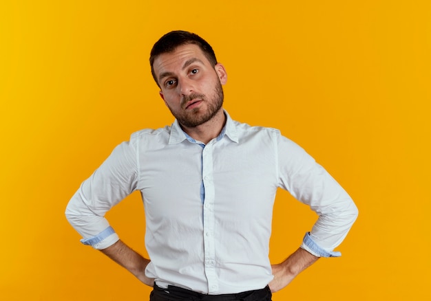 Confident handsome man puts hands on waist isolated on orange wall