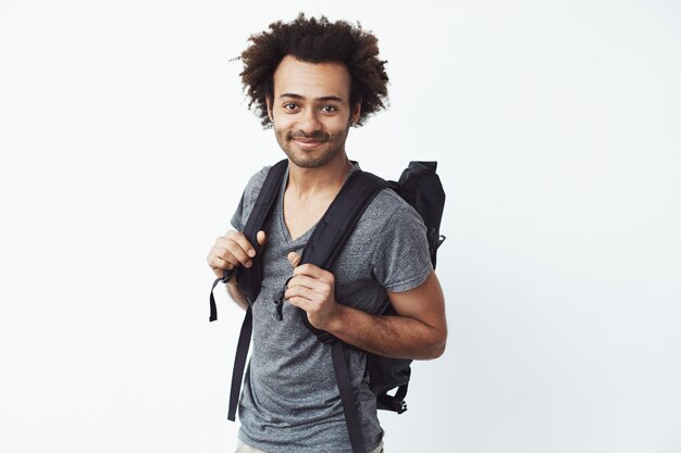 Уверенно и счастливый африканский молодой человек с усмехаться рюкзака готовый идти путешествовать автостопом или просто в горы.