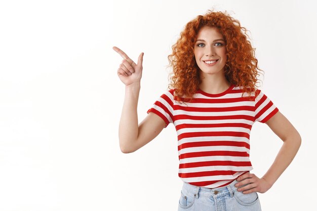 Confident happy curly redhead girl hold hand waist selfassured enthusiastic smiling broadly good mood pointing upper left corner assured assertive show best deal chip prices white background