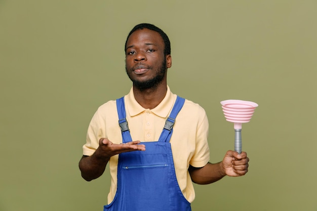 Free photo confident holding plunger young africanamerican cleaner male in uniform with gloves isolated on green background