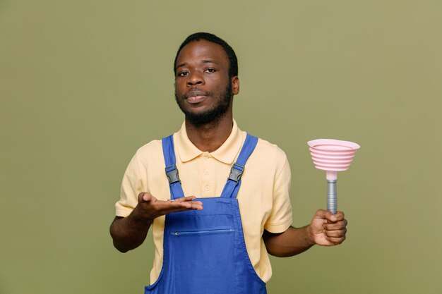 Confident holding plunger young africanamerican cleaner male in uniform with gloves isolated on green background