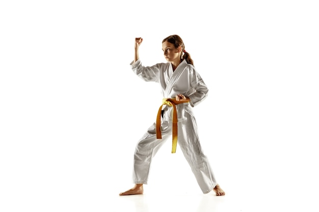 近接格闘術、武道を練習する着物の自信のあるジュニア。白い壁に黄色いベルトのトレーニングをしている若い女性の戦闘機。健康的なライフスタイル、スポーツ、アクションの概念。