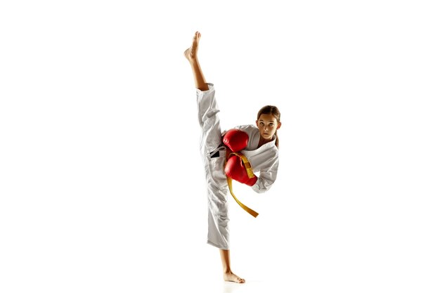 Confident junior in kimono practicing hand-to-hand combat, martial arts. Young female fighter with yellow belt s training on white  wall. Concept of healthy lifestyle, sport, action.